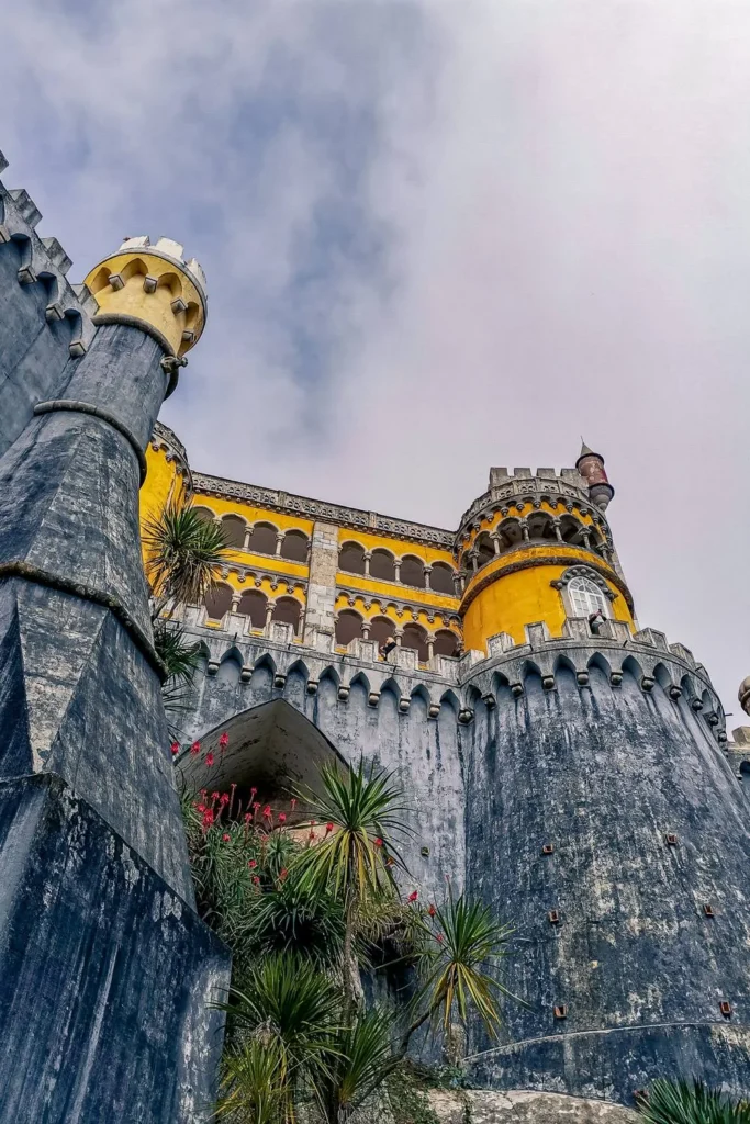 Colorful facade of the National Palace of Pena in Sintra, Portugal, viewed from below under a cloudy sky in February.