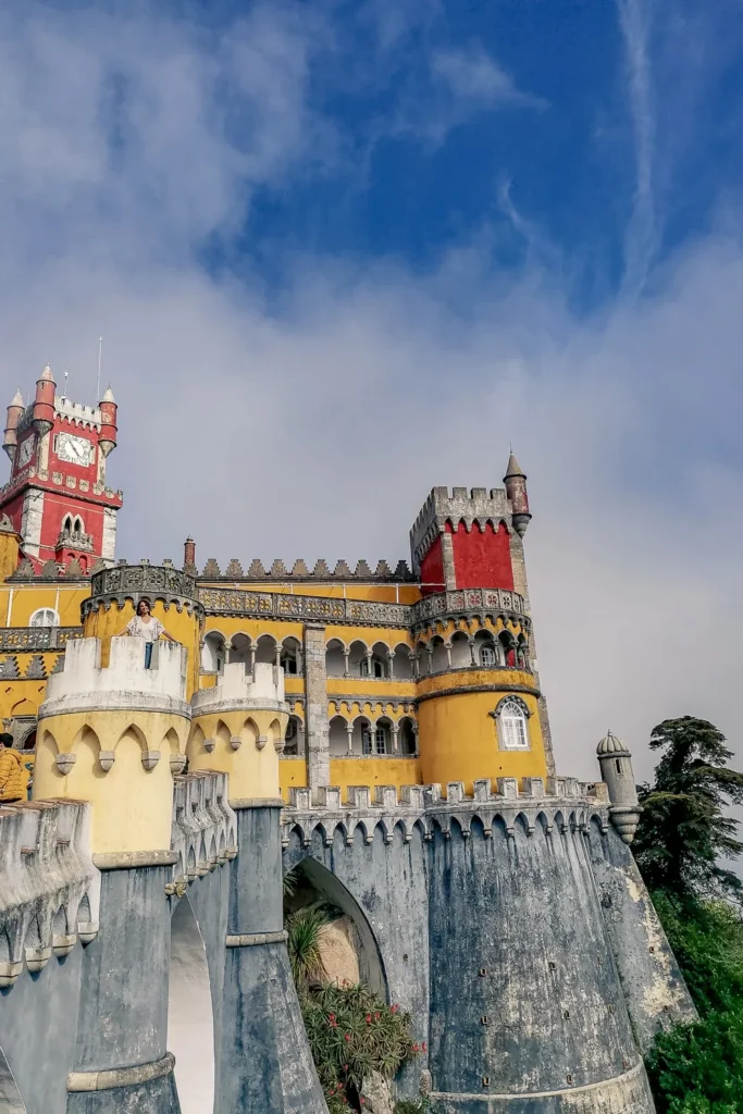 Colorful facade of the National Palace of Pena in Sintra, Portugal, with its characteristic yellow and red walls under a partially cloudy sky in February 2022.