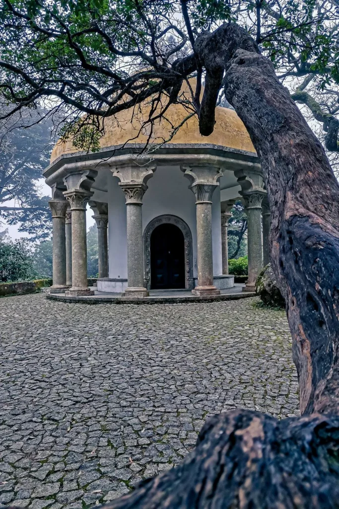 Small pavilion with a yellow dome surrounded by columns, located in the gardens of the Pena National Palace in Portugal, photographed in winter under a misty light.