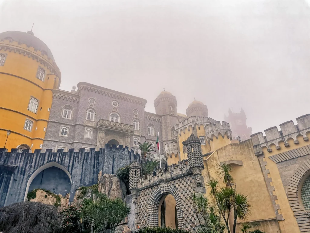 Facade of the Pena Palace in Portugal, partially shrouded in mist in March 2022. The colorful and eclectic architecture of the monument stands out in a mysterious atmosphere.