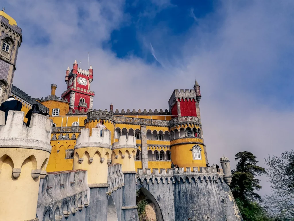 Colorful facade of the Pena Palace in Portugal, photographed in March 2022 under a partially cloudy sky.