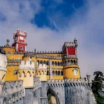 Colorful facade of the Pena Palace in Portugal, photographed in March 2022 under a partially cloudy sky.