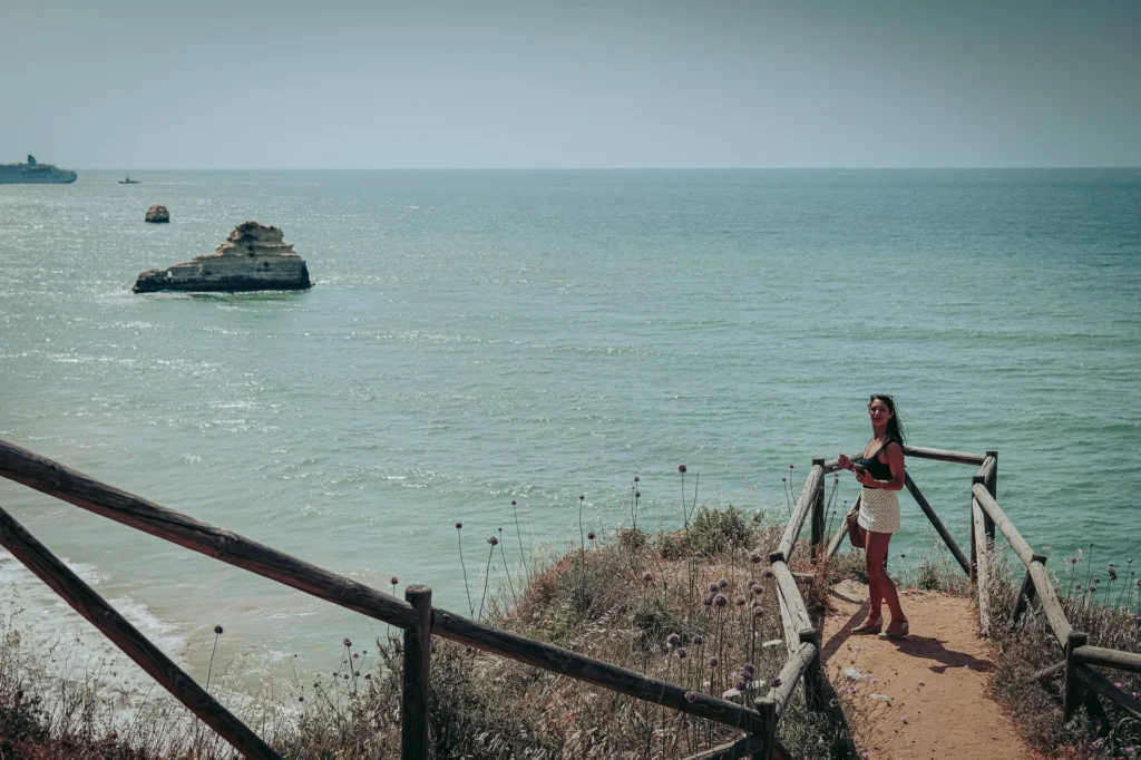 Caroline on a wooden path overlooking the Atlantic Ocean in Portimao, Algarve, under a clear sky in May.