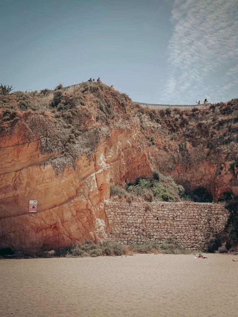 Large ochre cliff overlooking a sandy beach in Portimao, Algarve, under a clear sky in May.