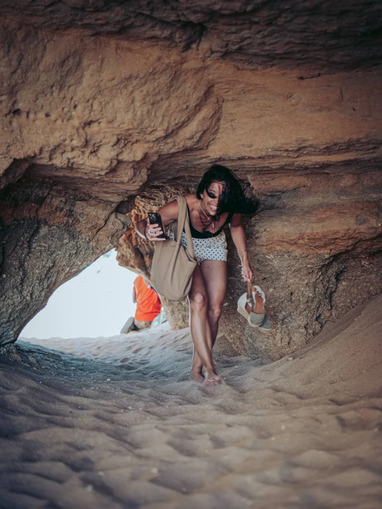 Caroline is crossing a small cave of sand and rock on a beach in the Algarve, Portugal, in May 2026.