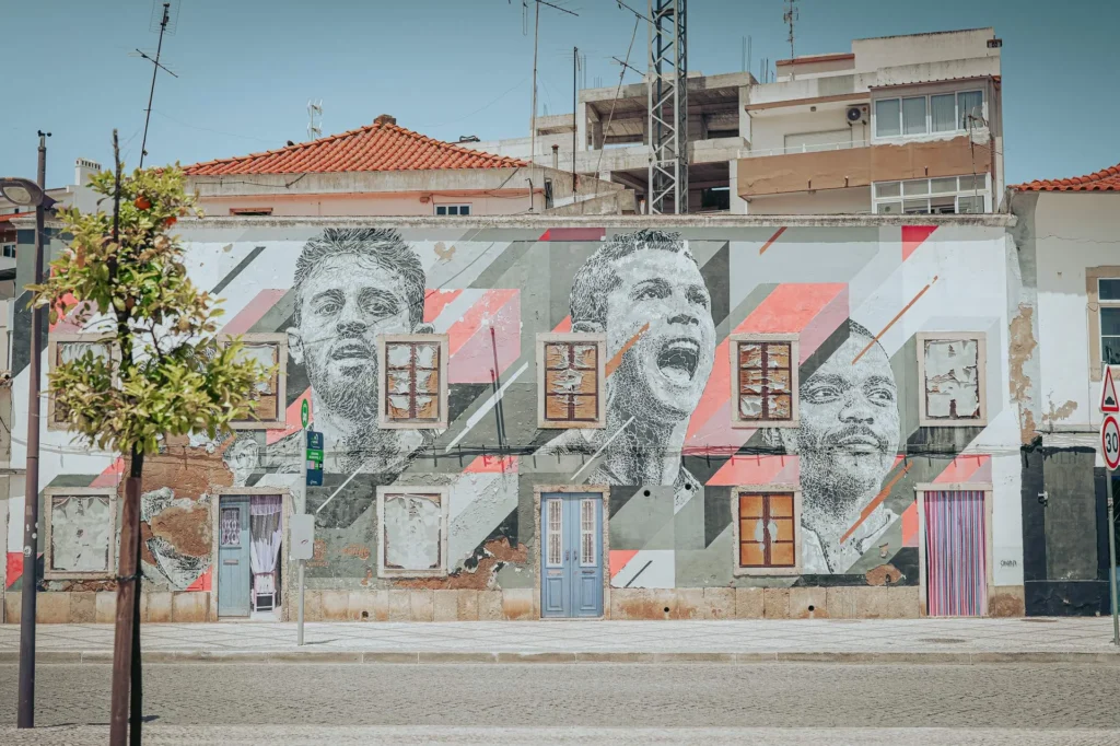 Mural depicting three male portraits on the facade of an old building in Portimao, under a clear sky.
