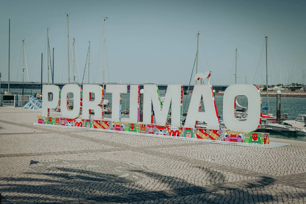 Large colorful letters spelling 'Portimao' on the waterfront, with sailboats moored in the background in Portimao, Algarve, Portugal in May 2026.