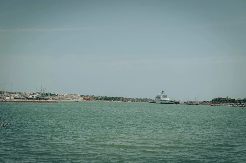 View of the Portimao harbor in the Algarve, with a large cruise ship docked and the town in the background under a clear sky.