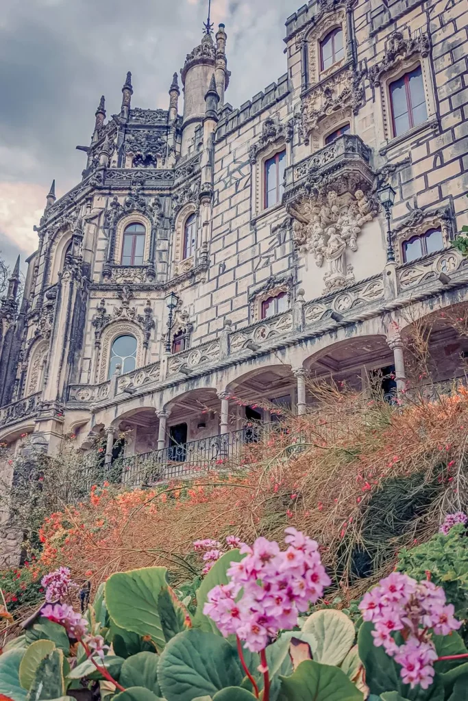 Ornate facade of the Quinta da Regaleira palace in Sintra, surrounded by flowers and vegetation in early spring 2022.