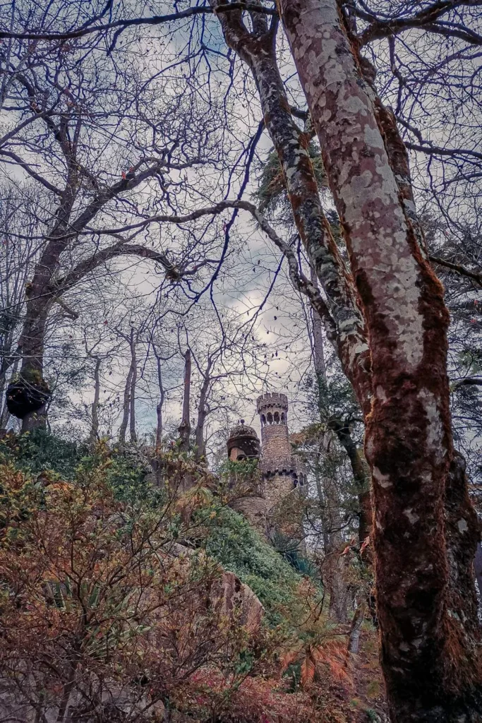 Gothic tower partially hidden by bare trees in the park of Quinta da Regaleira in Sintra, Portugal, in March 2022.