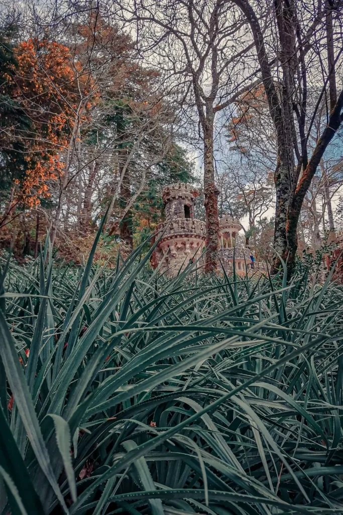 A stone tower in romantic style emerging from dense vegetation in the park of Quinta da Regaleira in Sintra, in early spring 2022.