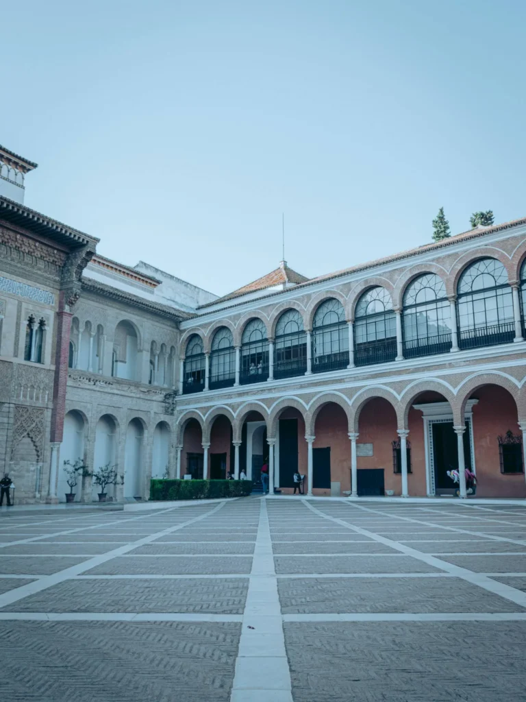 Cour intérieure du palais de l'Alcazar à Séville, architecture andalouse avec arcades et décorations mauresques sous un ciel dégagé.