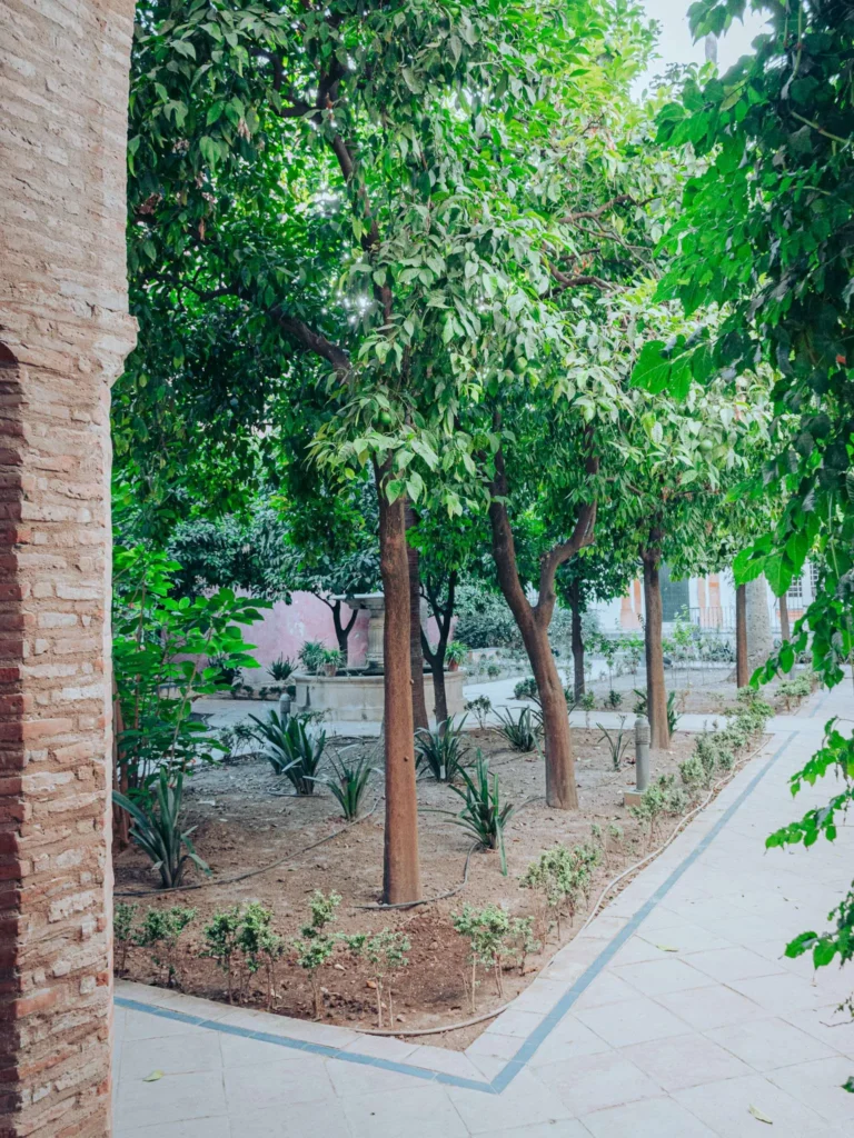 Jardin intérieur du palais Alcazar à Séville, avec des arbres et des plantations bordant une allée pavée, ambiance andalouse en octobre.