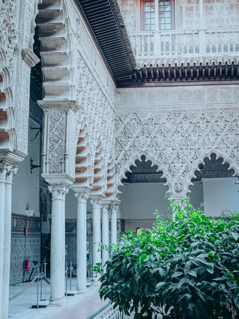 Cour intérieure du palais de l'Alcazar à Séville, avec des arches finement sculptées et une végétation centrale, ambiance andalouse historique.