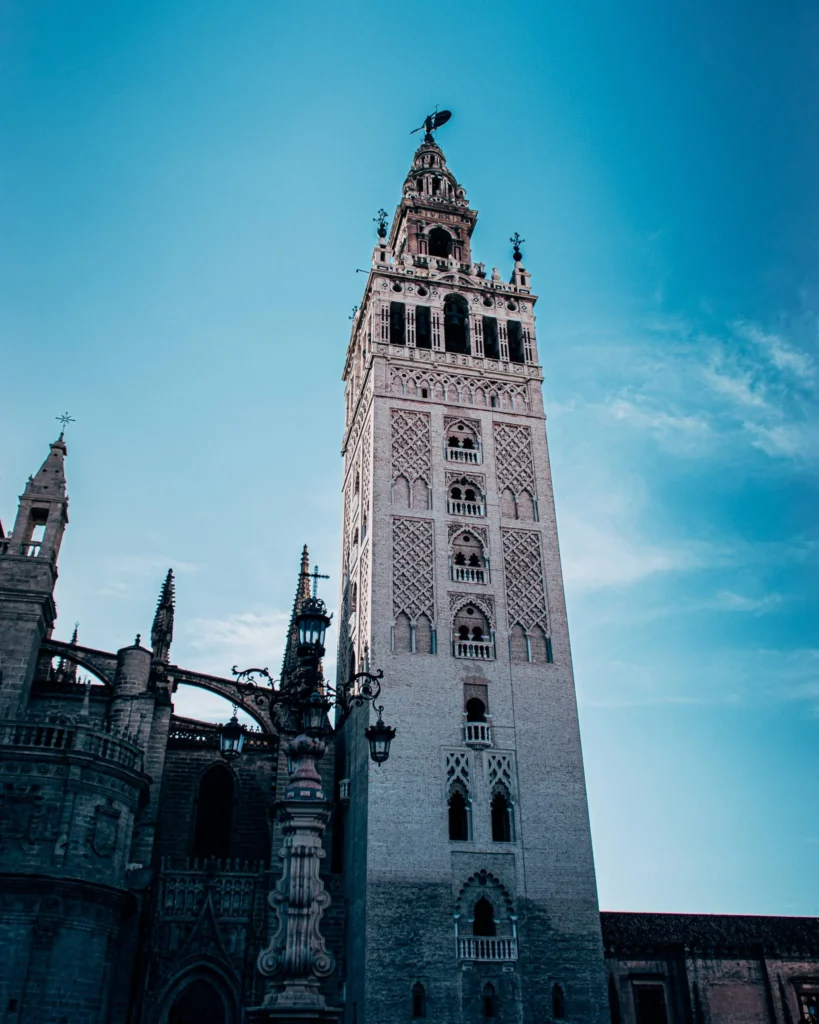 La Giralda de Séville se dresse sous un ciel bleu, mettant en valeur son architecture mauresque et gothique emblématique de l'Andalousie.