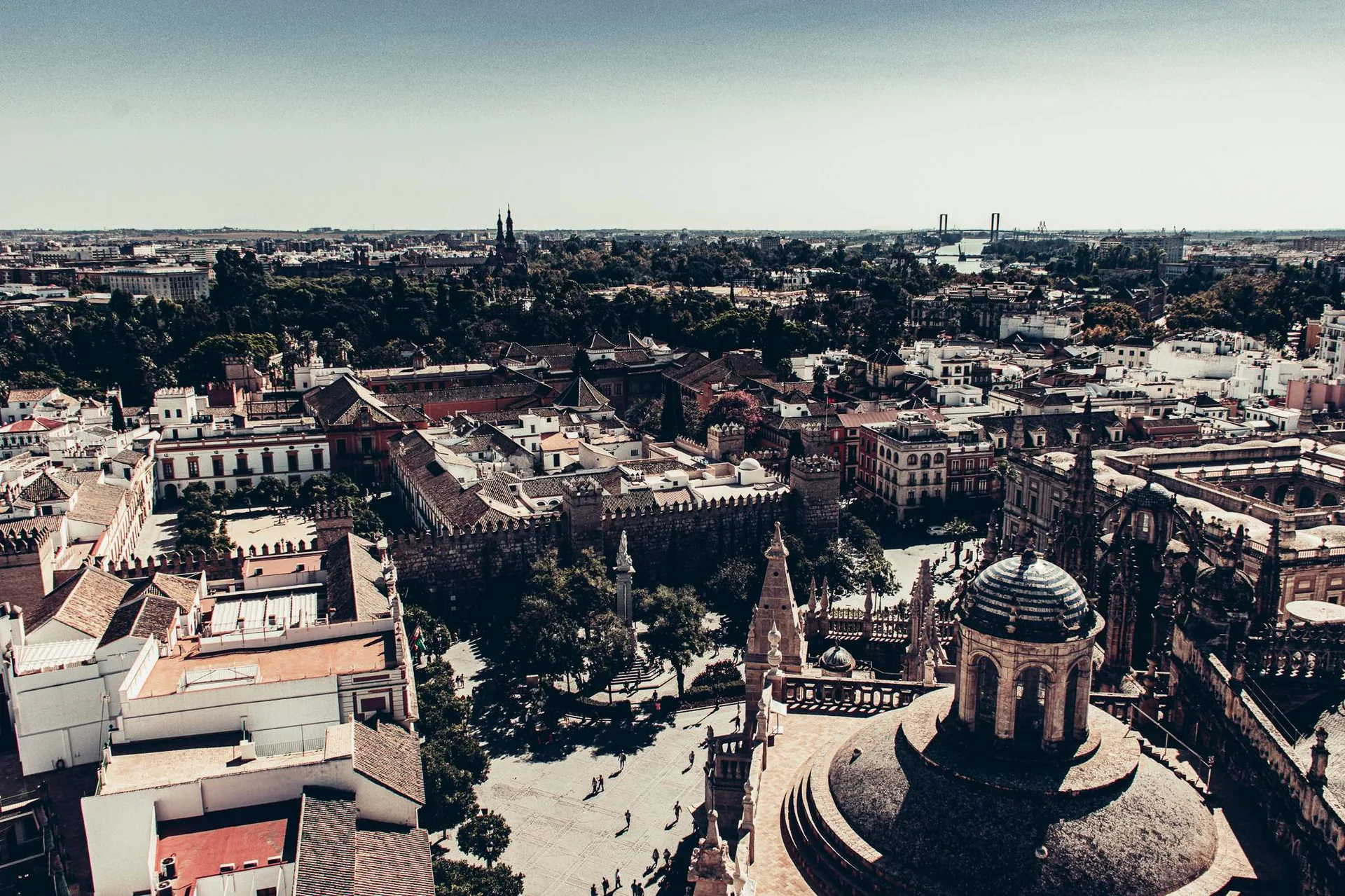 Vue panoramique sur le centre historique de Séville, avec la cathédrale et l'Alcazar visibles au premier plan sous un ciel dégagé.