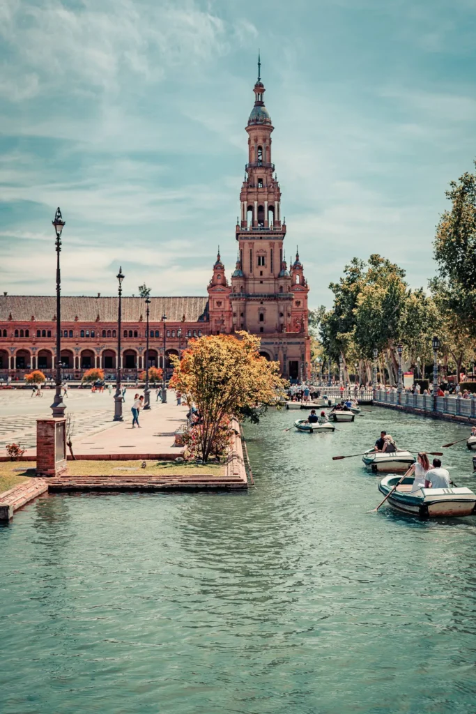 Vue de la Plaza de España à Séville avec sa tour emblématique, des barques sur le canal et des promeneurs sur l'esplanade par une journée ensoleillée d'octobre.