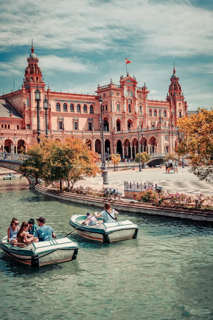 Barques de visiteurs sur le canal devant la Plaza de España à Séville, sous un ciel partiellement nuageux en automne.