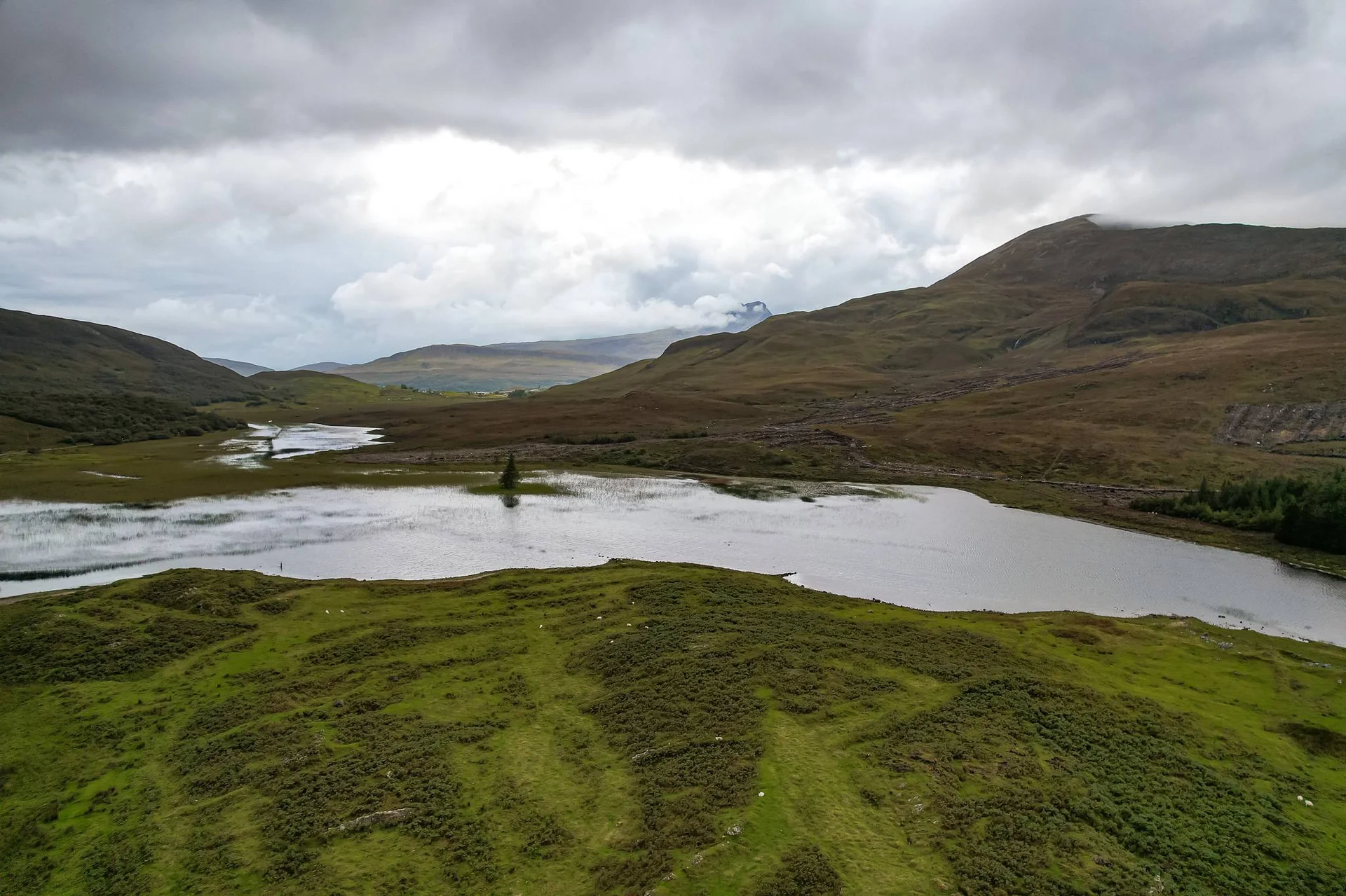 Rolling landscape of the Isle of Skye with a lake and green hills under a cloudy sky