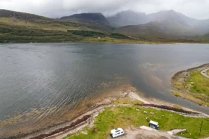 Aerial view of a loch on the Isle of Skye with a camper van parked by the water and misty mountains