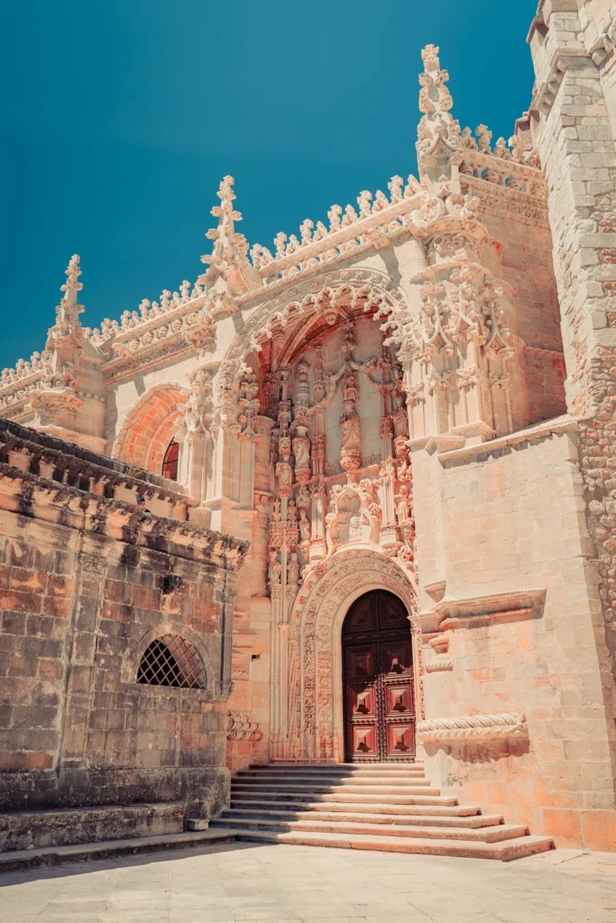 Façade monumentale du Couvent de l'ordre du Christ à Tomar, ornée de sculptures manuélines sous un ciel bleu en été.
