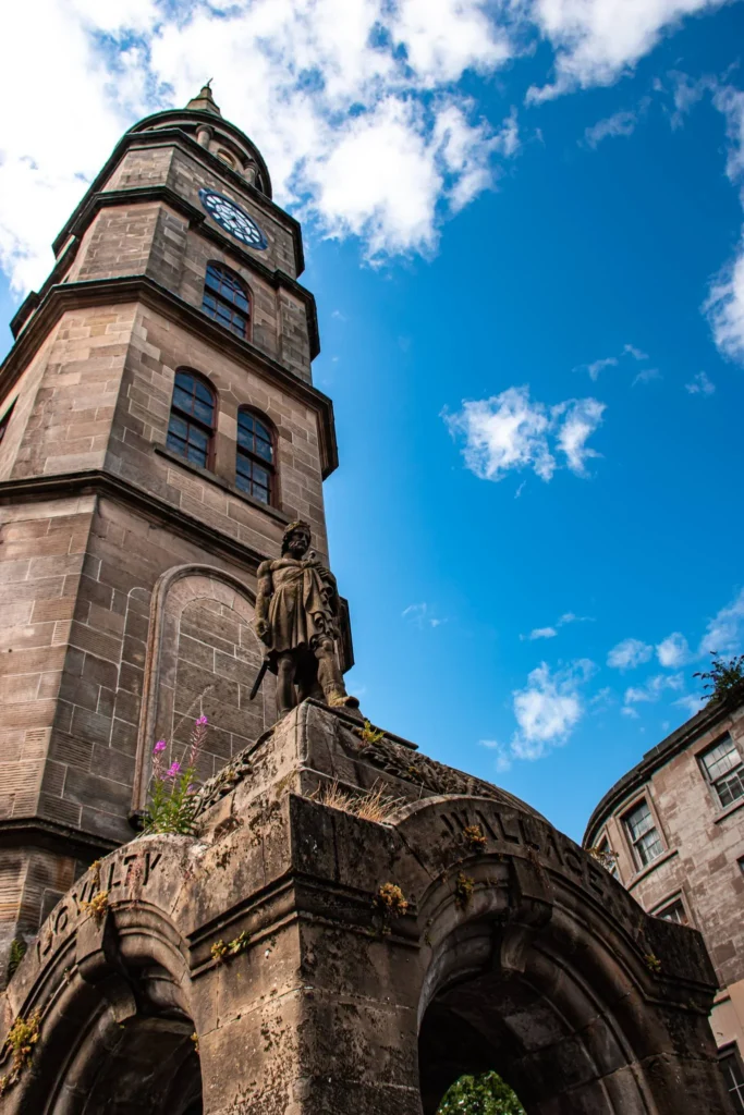 Historic stone tower with large clock and statue on a pedestal in Stirling