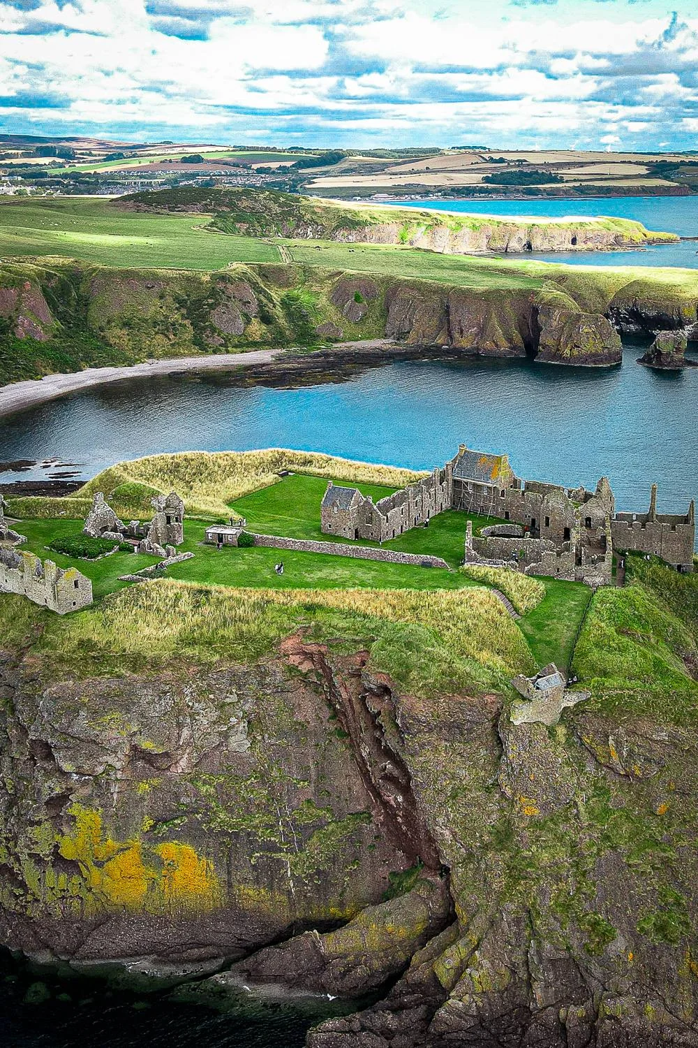 Aerial view of Dunnottar Castle perched on a green cliff overlooking the sea in Scotland