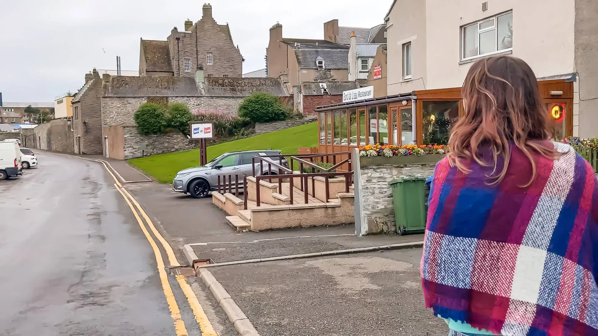 Caroline walks down a quiet street in Wick in front of a stone building restaurant.