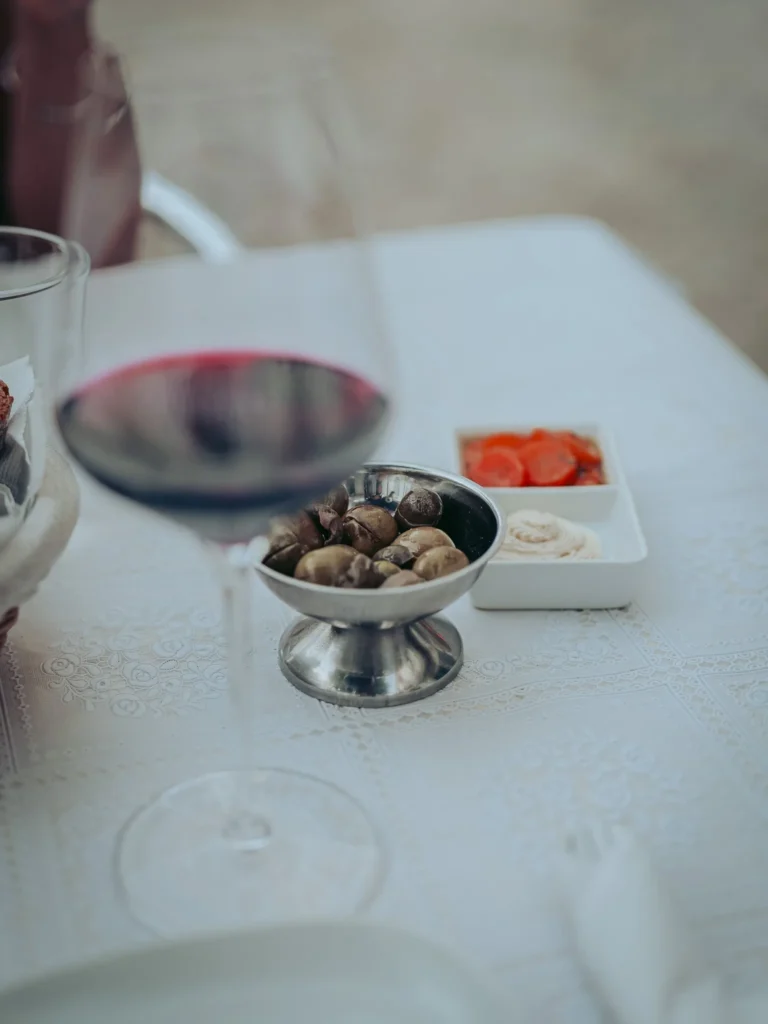 A glass of red wine, a bowl of olives, and appetizers (the Portuguese cutlery) are placed on a white tablecloth in a restaurant in Tavira, Algarve, Portugal, in June 2026.