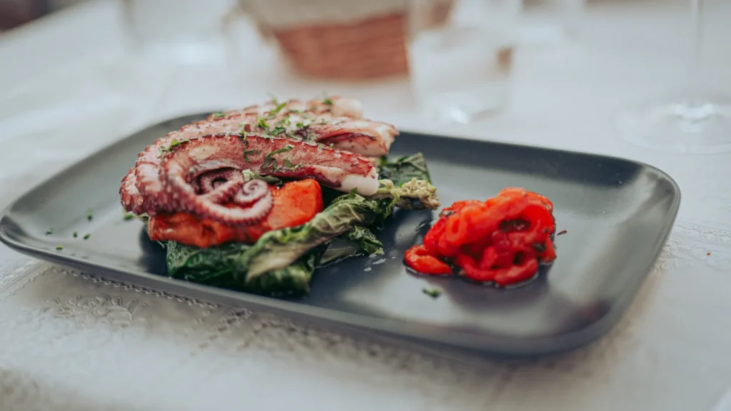 Octopus plate baked in the oven served with sweet potato and a roasted pepper salad on a set table in a restaurant in Tavira, Algarve.