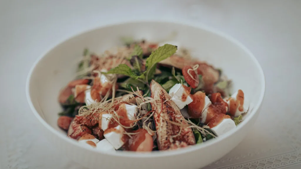 Grilled fig salad with fresh cheese, herbs, and sprouts served on a white plate on a light tablecloth at Case de Pasto restaurant in Tavira, Algarve.