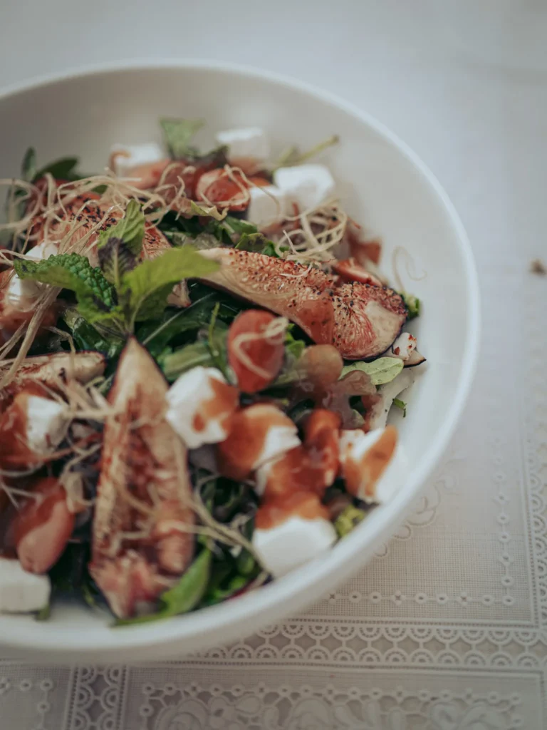 Grilled fig salad with fresh cheese, sprouts, and fresh herbs served on a white plate on an embroidered tablecloth at Case de Pasto restaurant in Tavira, Algarve.