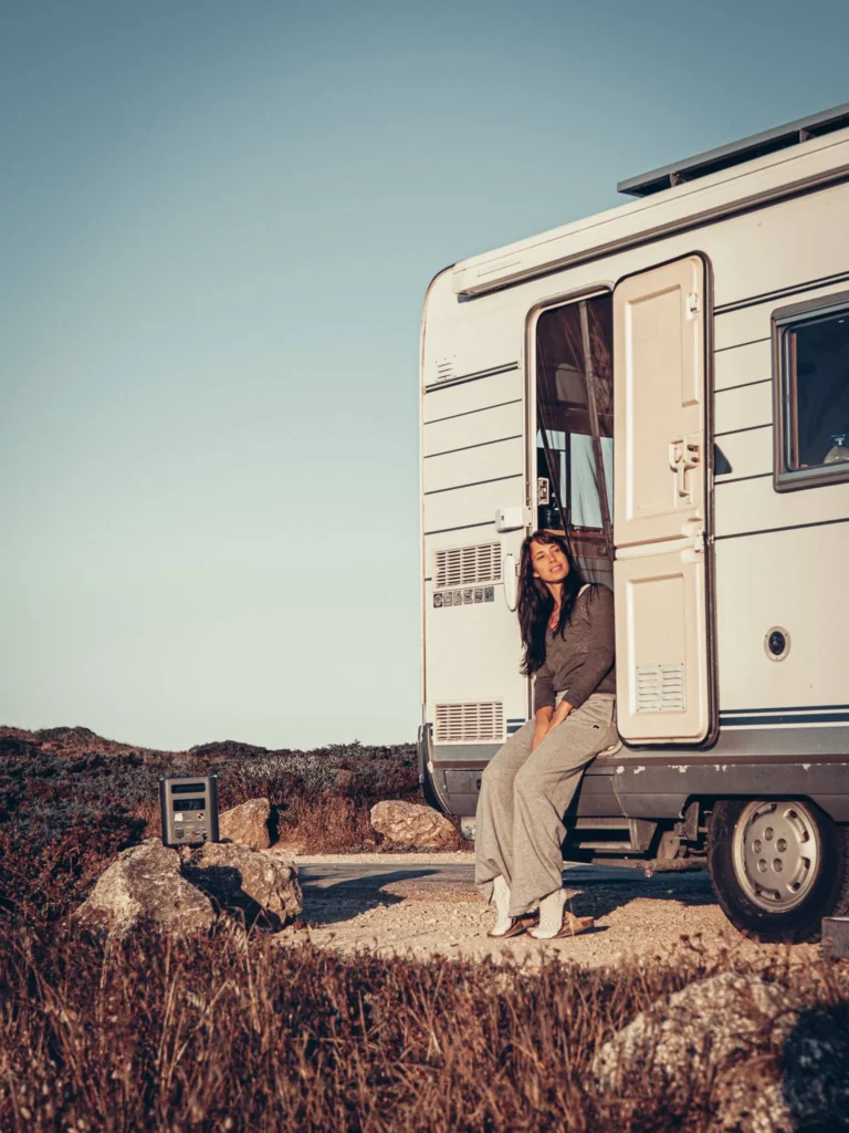 Caroline sitting at the entrance of the camper van in the heart of nature with the Aferiy Nomad 1800 station nearby