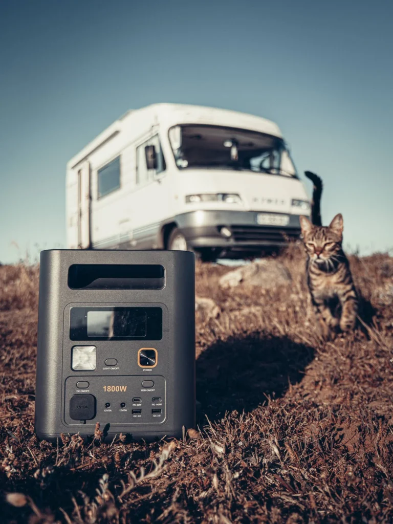 Close-up of the Aferiy Nomad 1800 station on the grass, with the cat Vasco nearby and the camper van in the background.