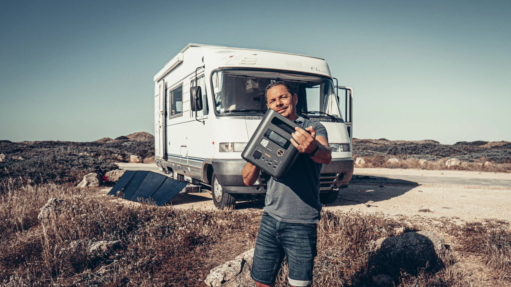 Xavier holding the portable power station Aferiy Nomad 1800 in front of the camper van Édouard, solar panel deployed in the great outdoors