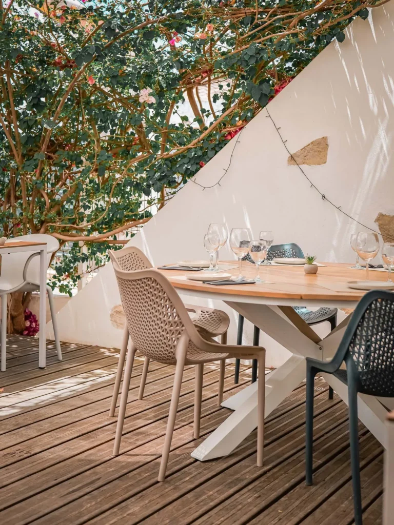 Tisch gedeckt auf der holzverkleideten Terrasse des Restaurants Coisa Linda in Tavira, unter einer blühenden Pergola und natürlichem Licht.