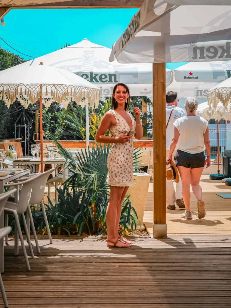 Caroline steht auf der Terrasse im Restaurant Coisa Linda in Tavira, unter Heineken-Sonnenschirmen, an einem sonnigen Tag.