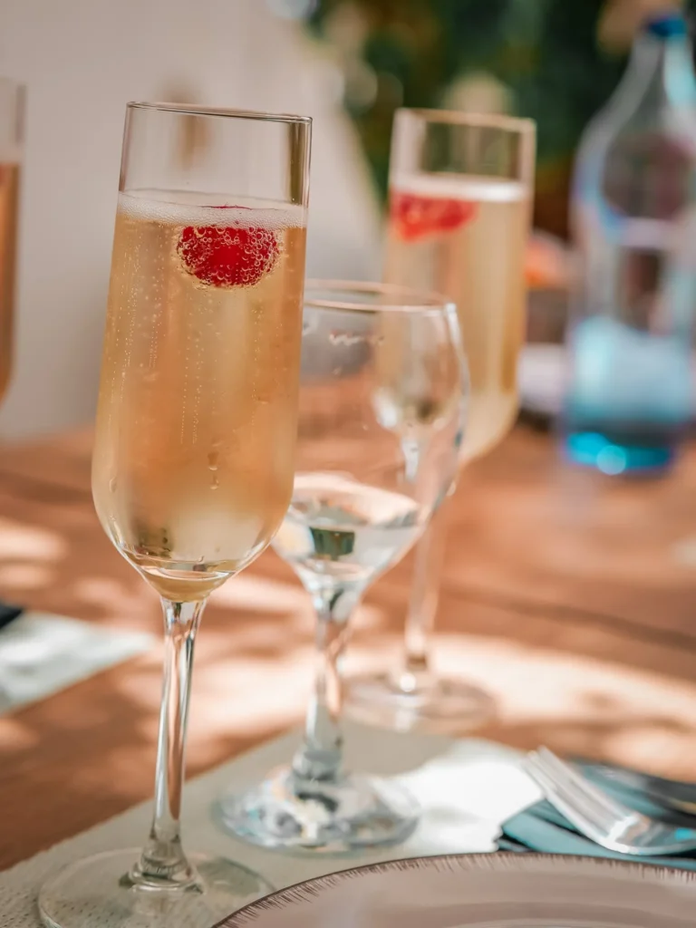 Champagnergläser mit einer Himbeere, serviert auf einem gedeckten Tisch auf der Terrasse im Restaurant Coisa Linda in Tavira, Algarve, an einem sonnigen Tag Ende Mai.