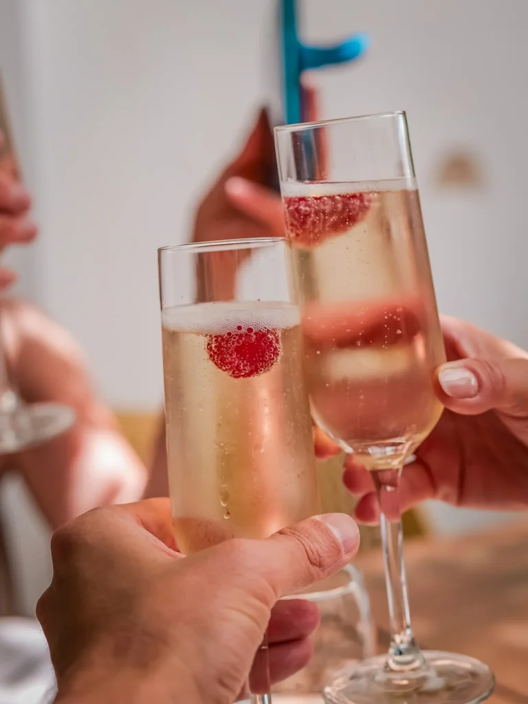 Champagnergläser mit einer Himbeere darin, die für einen Toast in einer sommerlichen Atmosphäre im Restaurant Coisa Linda in Tavira, Algarve, erhoben werden.