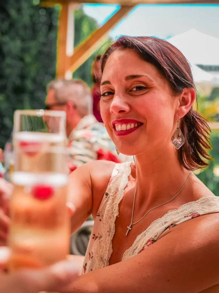 Caroline lächelt auf der Terrasse des Restaurants Coisa Linda in Tavira, Algarve, mit einem Glas in der Hand an einem sonnigen Tag.