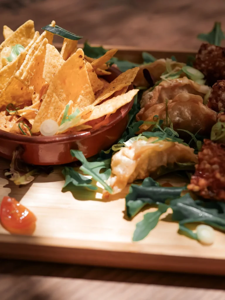 Auswahl an Nachos, Gyozas und Rucolablättern, serviert auf einem Holzbrett in einem Restaurant in Tavira, Algarve, im Mai 2026.