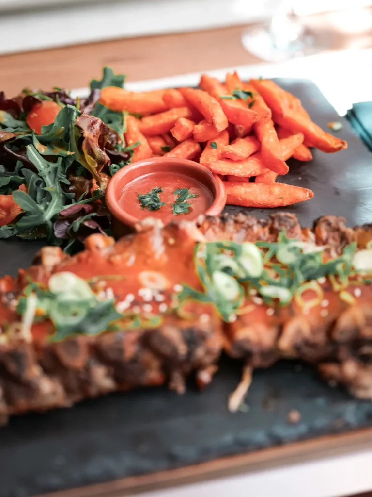 Schweinerippchen in Sauce, serviert mit Süßkartoffel-Pommes, grünem Salat und Sauce, im Restaurant Coisa Linda in Tavira.