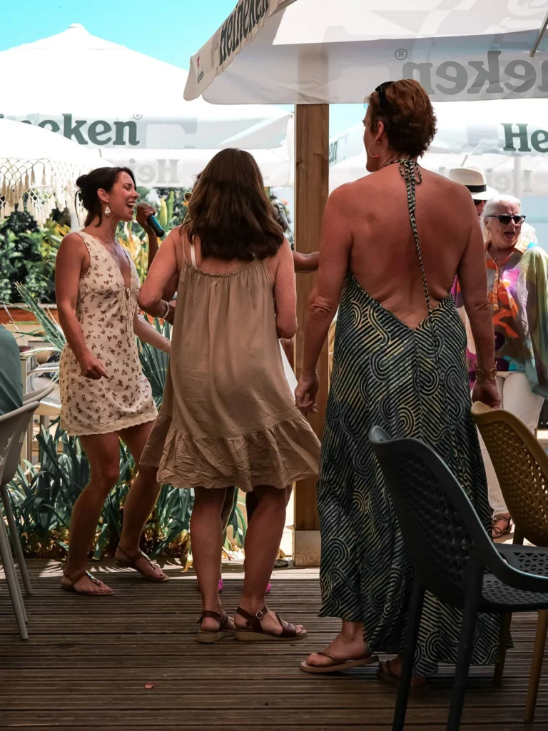 Caroline und andere Frauen diskutieren und lachen auf der Terrasse unter Sonnenschirmen in einer sommerlichen Atmosphäre im Restaurant Coisa Linda in Tavira.