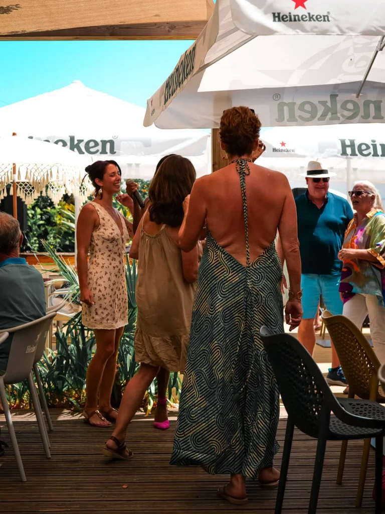 Sommerliche Atmosphäre auf der Terrasse eines Restaurants in Tavira, mit mehreren Erwachsenen in leichter Kleidung unter Heineken-Sonnenschirmen.