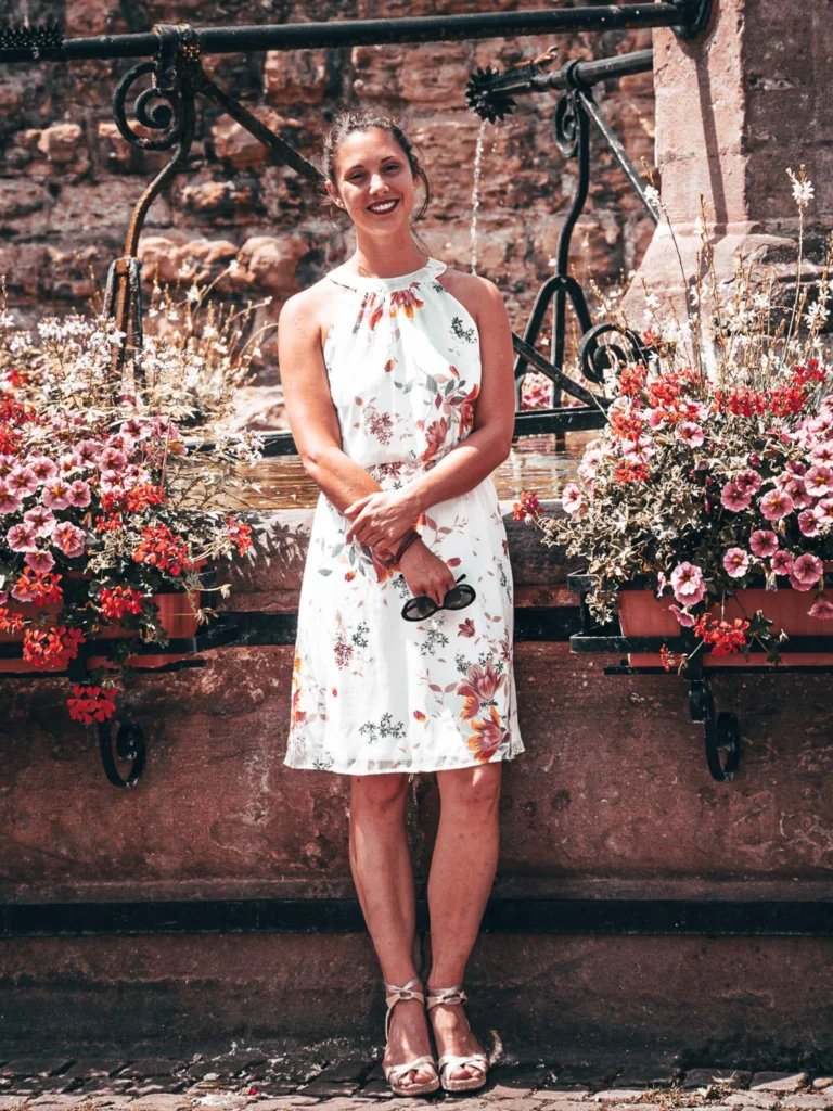Caroline in front of a flowered stone fountain in a alley of Eguisheim