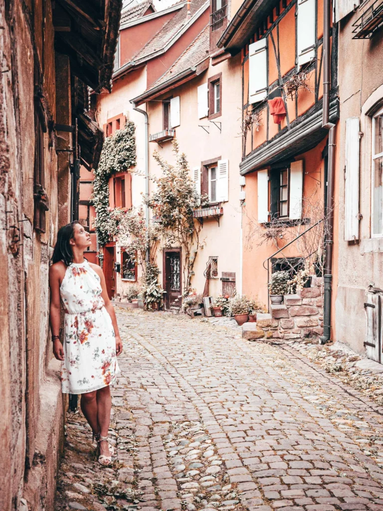 Caroline in a cobbled alley lined with colorful half-timbered houses in Eguisheim