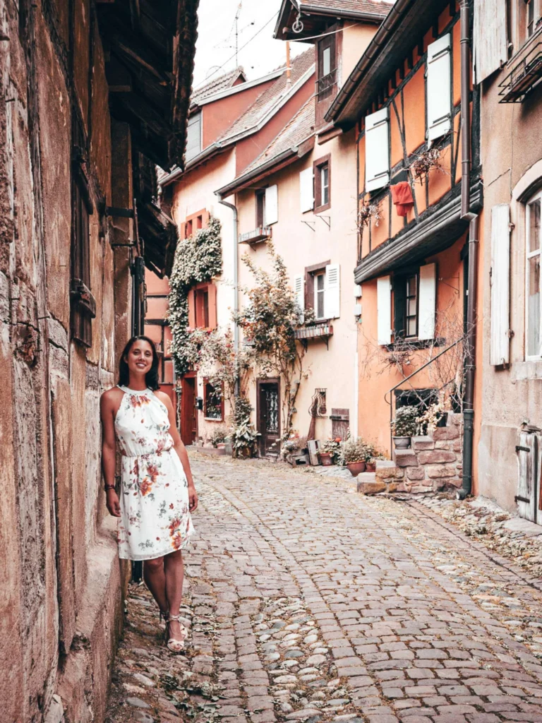 Caroline strolling in a cobbled alley of Eguisheim between the half-timbered houses