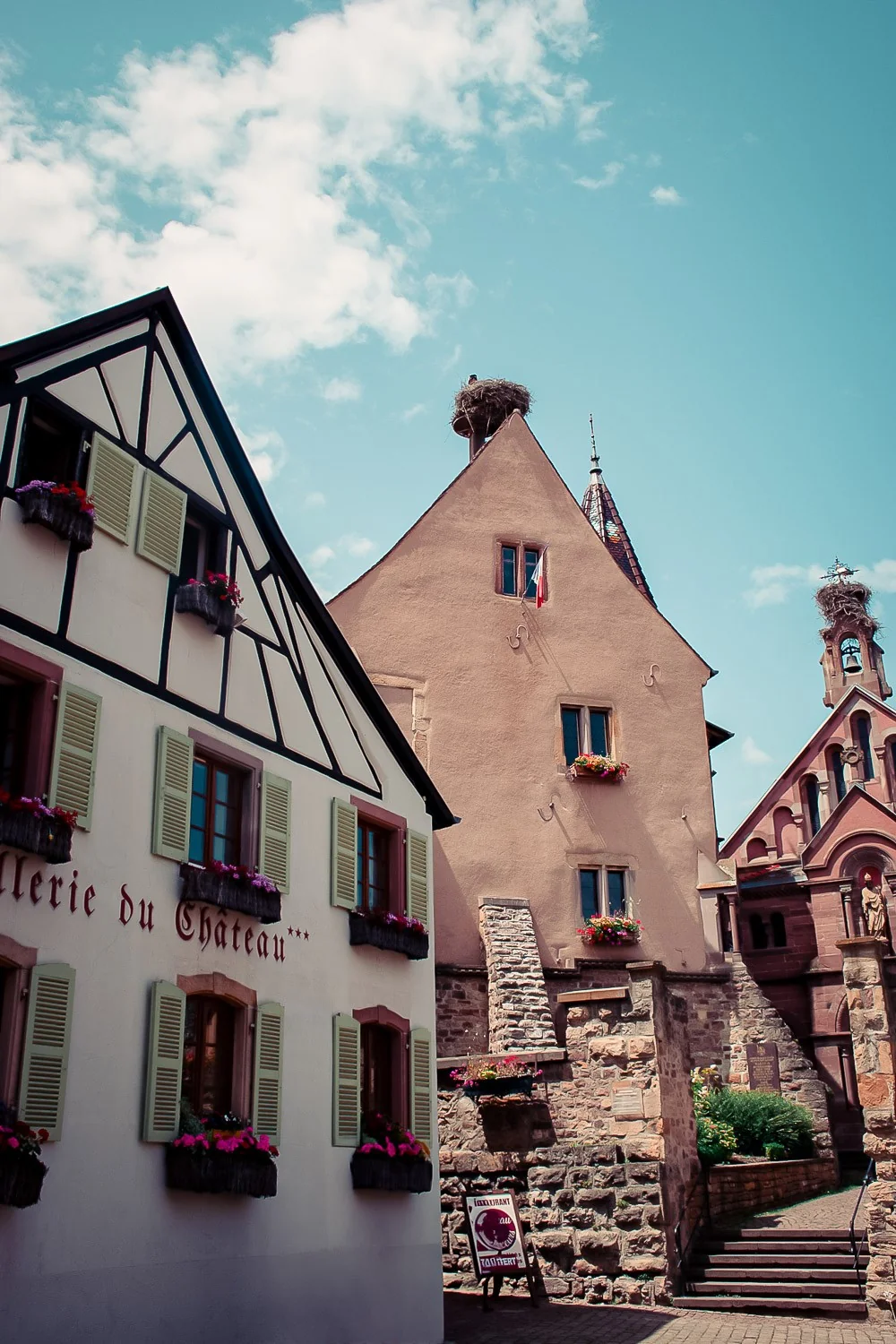 Half-timbered houses adorned with flowers and traditional Alsatian buildings in Eguisheim under a blue sky