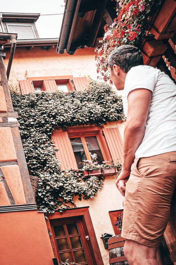 Xavier in a picturesque alley of Eguisheim in Alsace, observing a half-timbered facade