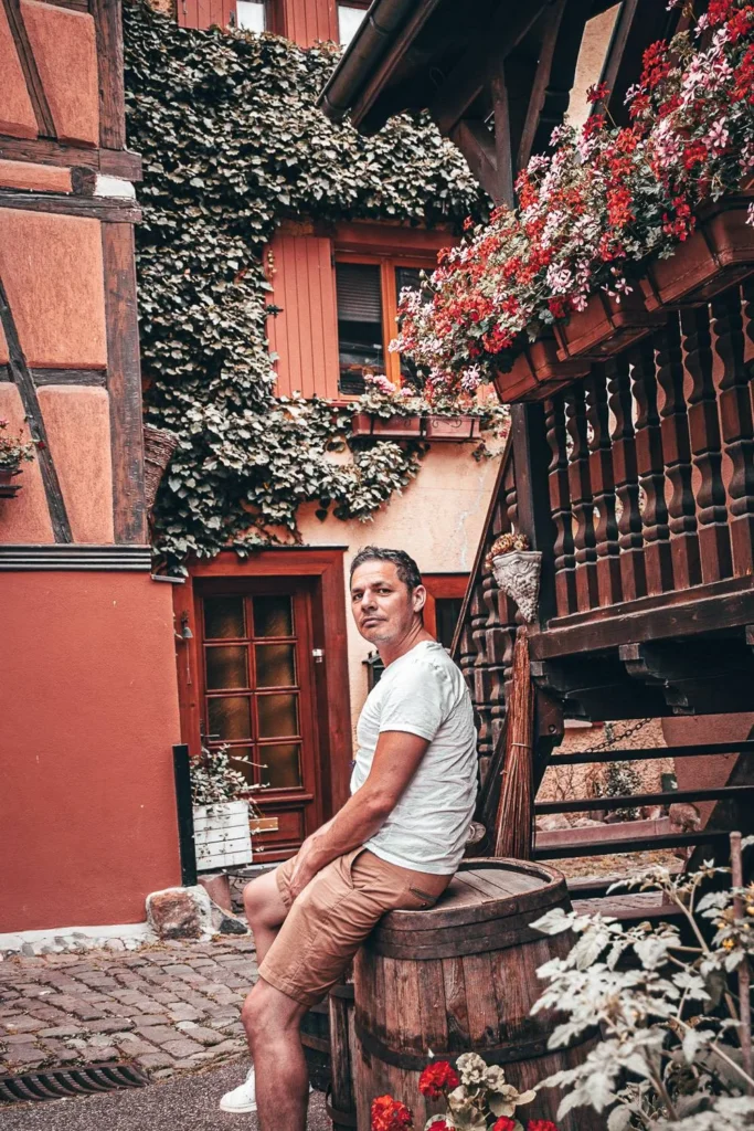 Xavier sitting on a barrel in a picturesque alley of Eguisheim, ambiance Alsace Wine Route
